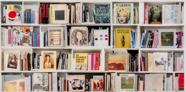 A wall of colorful book covers on shelves, displaying art, portraits, and magazines in a bookstore or library.