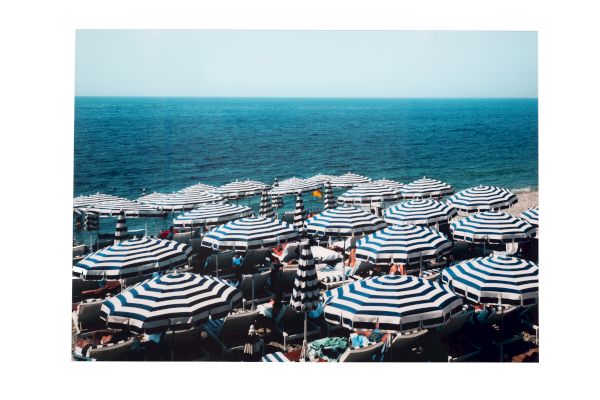 A crowded beach with many striped umbrellas facing the ocean.