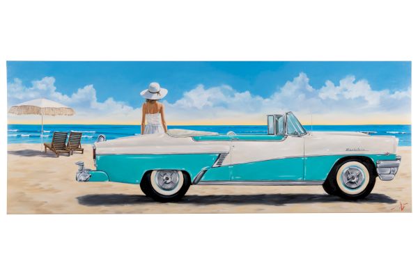 A retro turquoise and white convertible on a sandy beach, with a woman in a white hat standing beside it, blue sky and ocean behind.